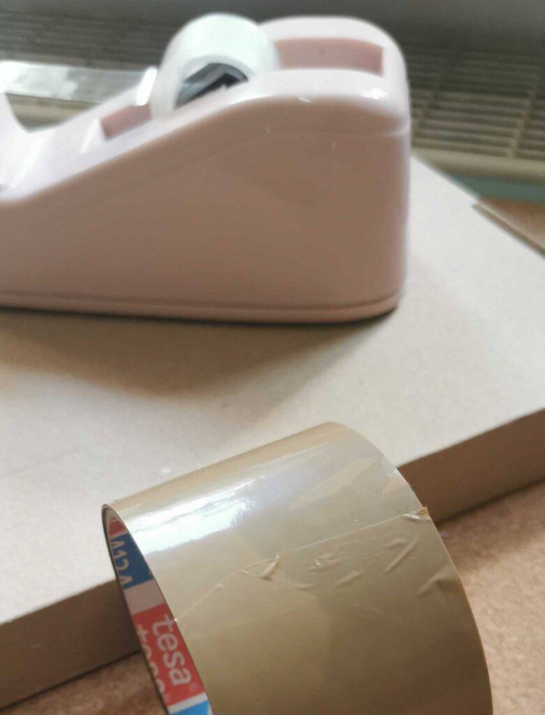 Ansicht von oben auf ein braunes getestetes Paketklebeband, das vor einem weißen Klebebandabroller liegt.