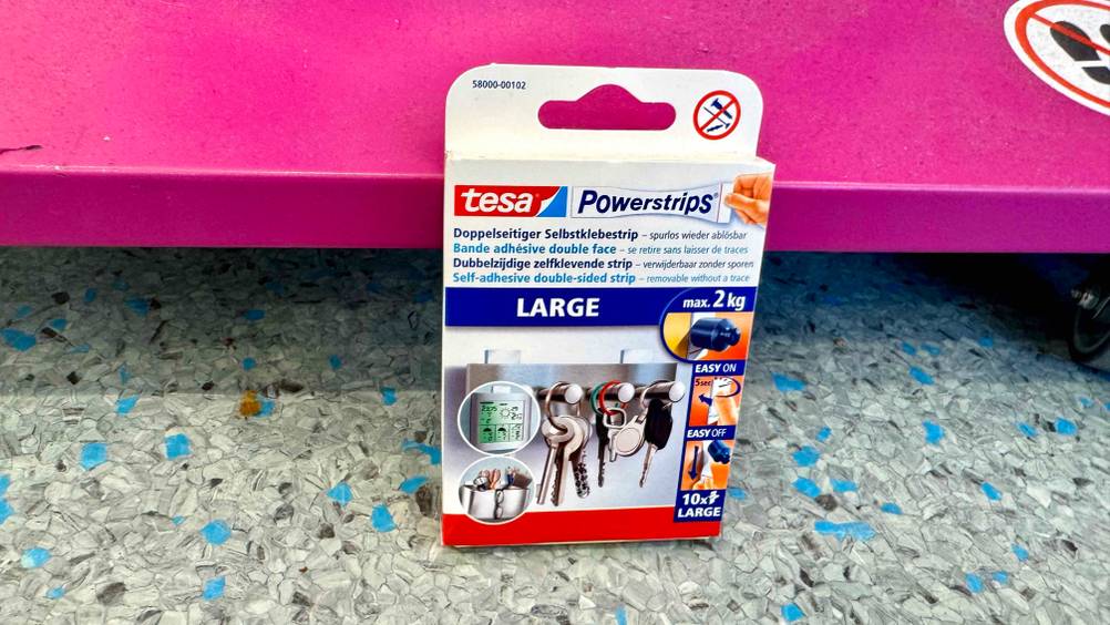Die getesteten Tesa-Powerstrips lehnen an einem rosa Regal.