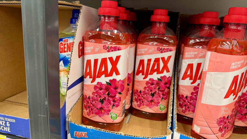 Getestet: Ajax-Allzweckreiniger in der Kunststoffflasche mit roter Flüssigkeit steht in Kartons auf einem Verkaufsregal.