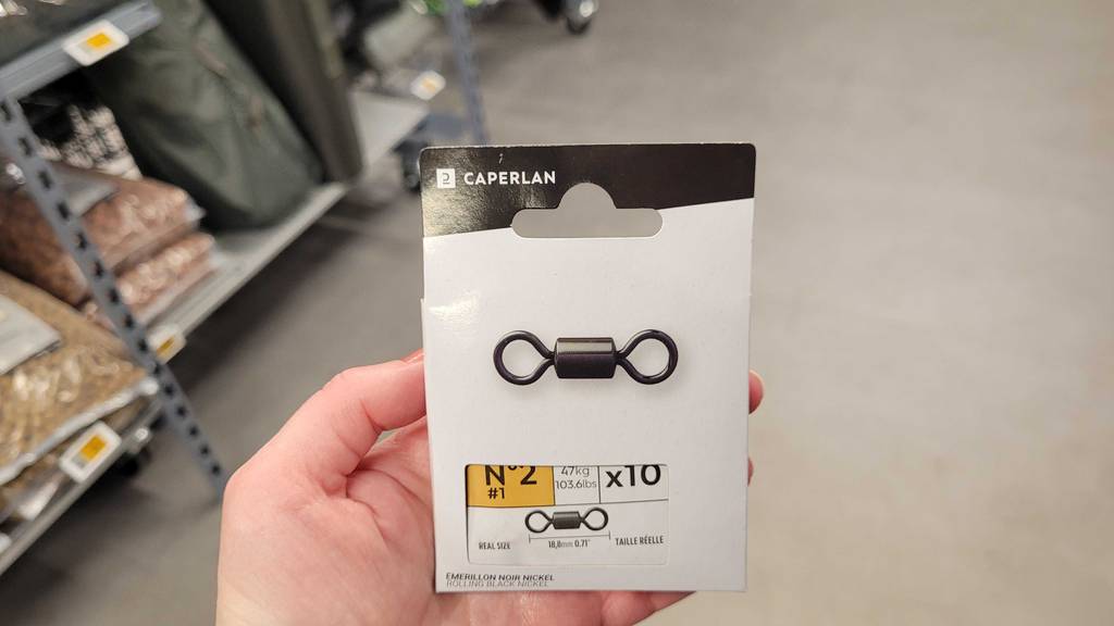 Eine Hand hält eine Verpackung mit 10 Stück Angelwirbel im Test vor einem Verkaufsregal.