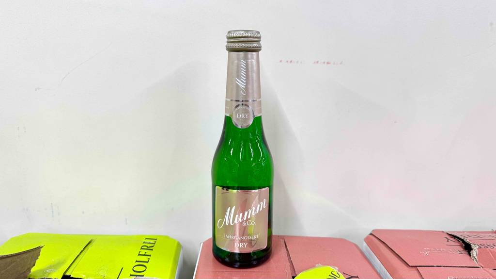Eine Portionsflasche mit getestetem Mumm Sekt steht auf einem Getränkekarton.
