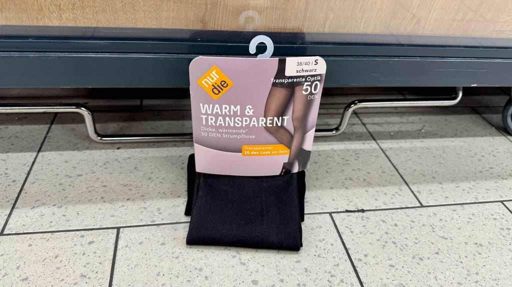 Eine getestete Nur-Die-Strumpfhose in Schwarz lehnt an einem grauen Warenbehälter auf Rollen.