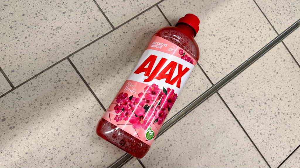 Getesteter Ajax-Allzweckreiniger in einer Kunststoffflasche mit roter Flüssigkeit liegt auf einem Fliesenbelag.