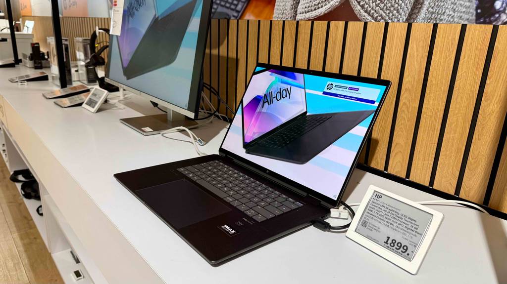 Laptop-Windows-11 getestet: Ein geöffnetes Modell steht mit eingeschaltetem Bildschirm neben dem Preisschild auf einer Ausstellungsfläche.