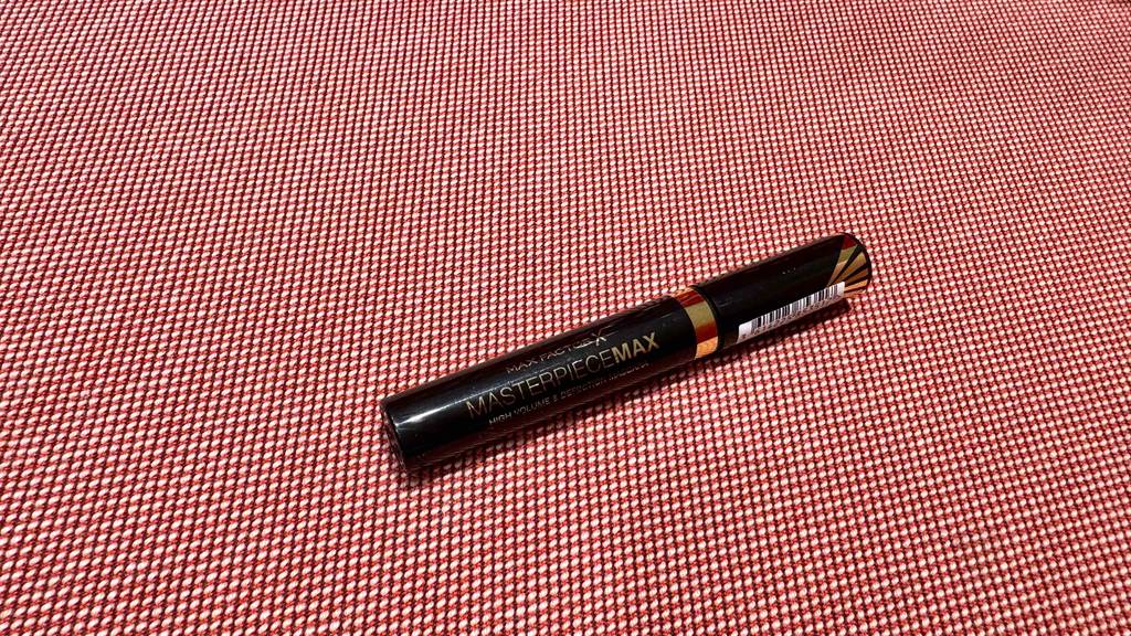 Ein schwarzer Stift mit Max-Factor-Mascara im Test liegt auf einer roten Oberfläche.