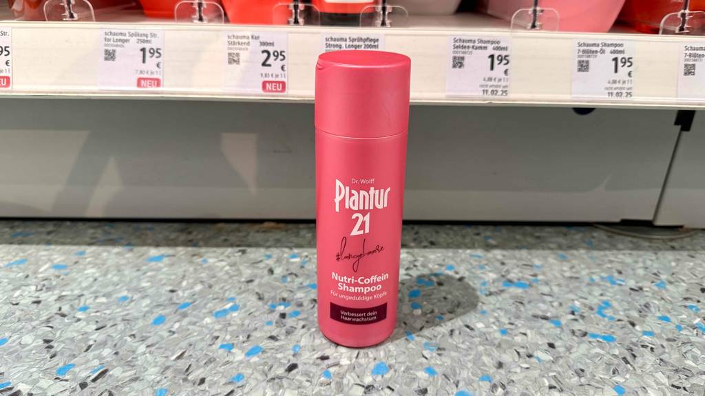 Vor einem Verkaufsregal mit Preisschildern steht das getestete Plantur-Shampoo in der roten Kunststoffflasche.