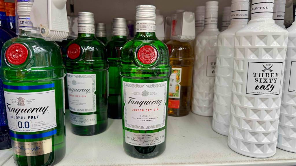 Tanqueray-Gin-Test: Mehrere grüne Flaschen mit Schraubverschluss stehen nebeneinander in einem Verkaufsregal im Supermarkt.