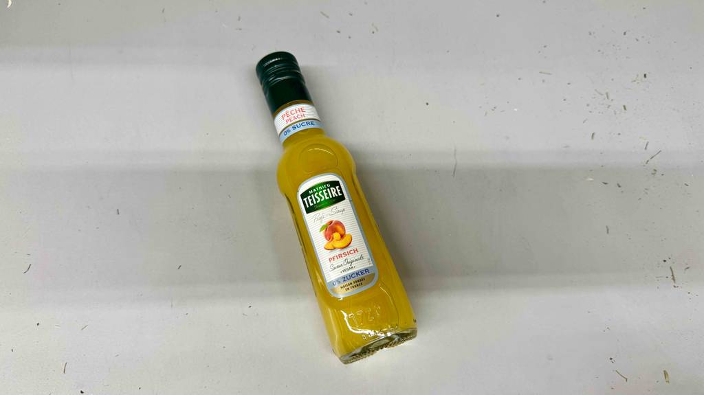 Teisseire-Sirup im Test: Die Flasche mit gelber Flüssigkeit liegt auf einem weißen Untergrund.