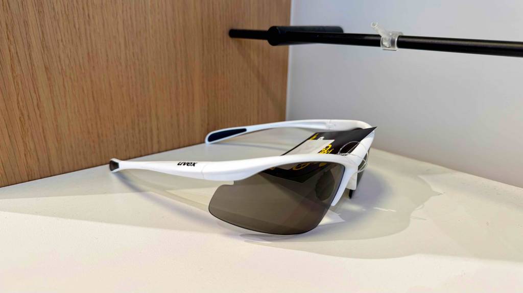 Getestet: Eine Uvex-Fahrradbrille mit getönten Gläsern und weißem Halbrand liegt auf einem weißen Ausstellungsregal.