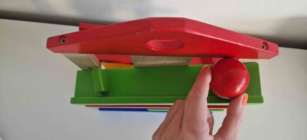 Nahaufnahme von oben von einer bunten Holz-Kugelbahn im Test inklusive Hand, die eine rote Holzkugel hält.
