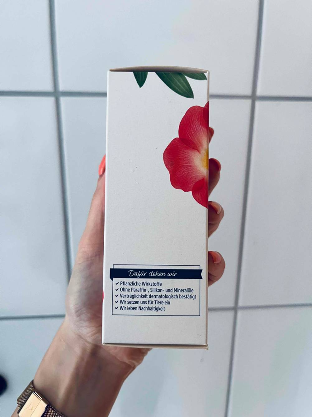 Eine Hand hält eine Packung der getesteten Teufelskralle seitlich vor eine Fließenwand.