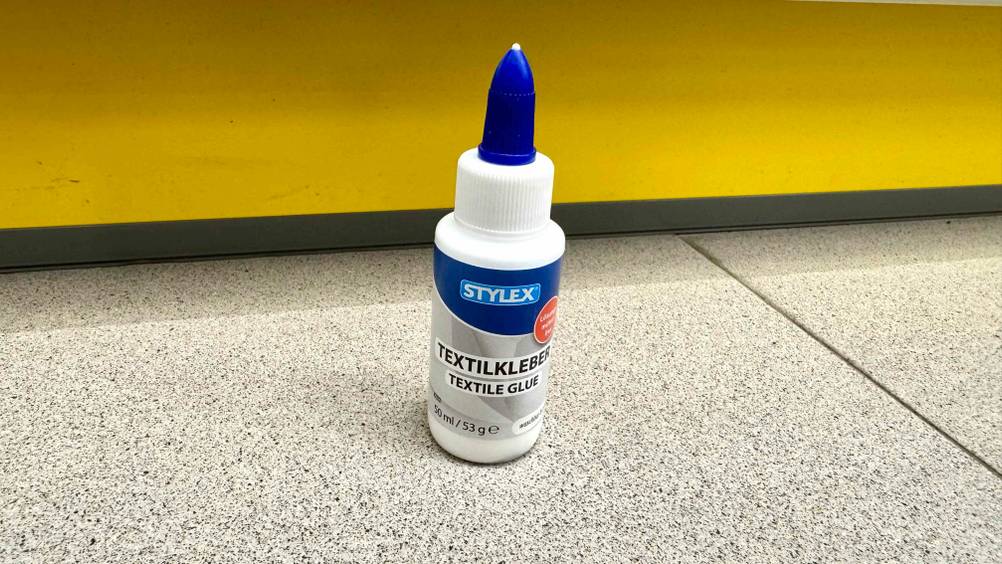 Vor einer gelben Fläche steht ein Textilkleber im Test auf dem Boden.