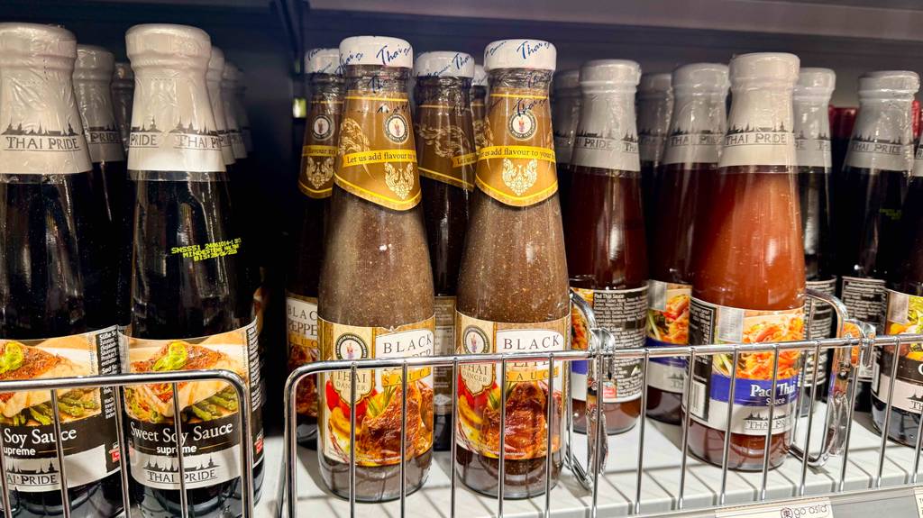 Pfeffersauce im Test: Mehrere Flaschen stehen hinter- und nebeneinander zwischen anderen Saucen in einem Regal.