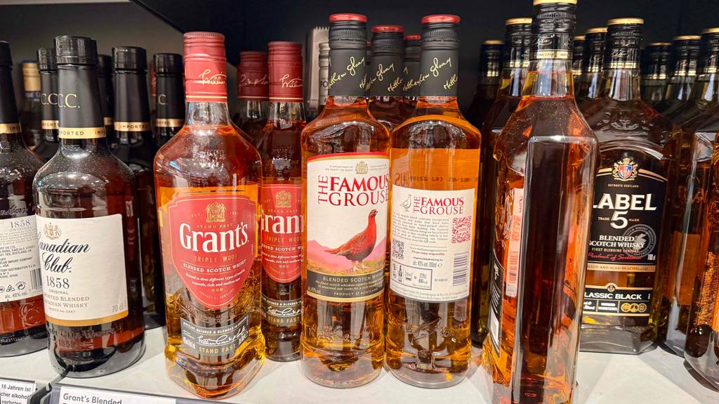 Blended Whisky im Test: Mehrere Flaschen, eine davon mit der Rückseite nach vorn, stehen zwischen anderen Sorten in einem Regal.