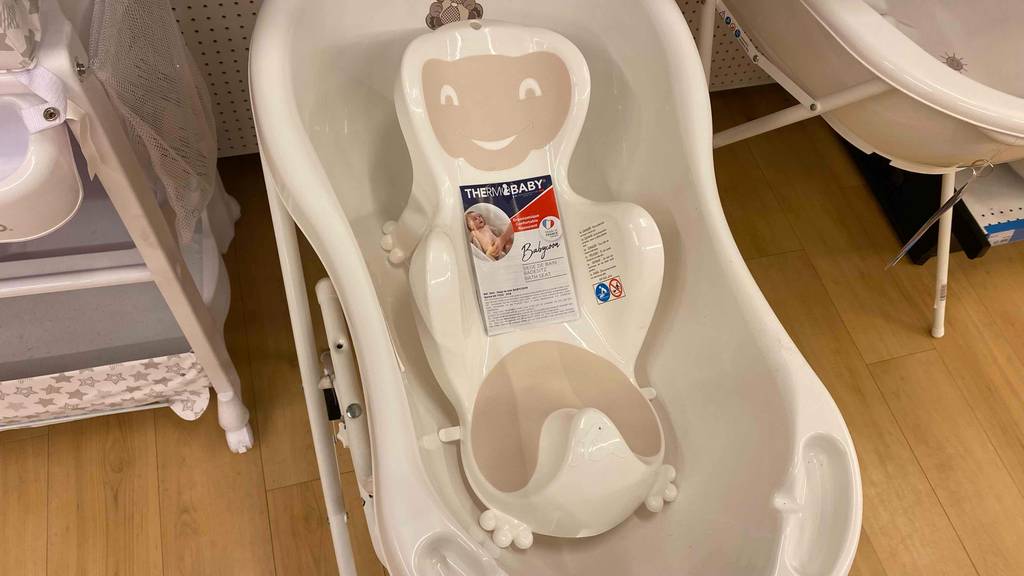 Ein beigefarbener Baby-Badewannensitz im Test in stilisierter Bärenform steht auf seinen Saugnapf-Füssen in einer hellen Kinderbadewanne inklusive Gestell, die in einem Geschäft ausgestellt ist.