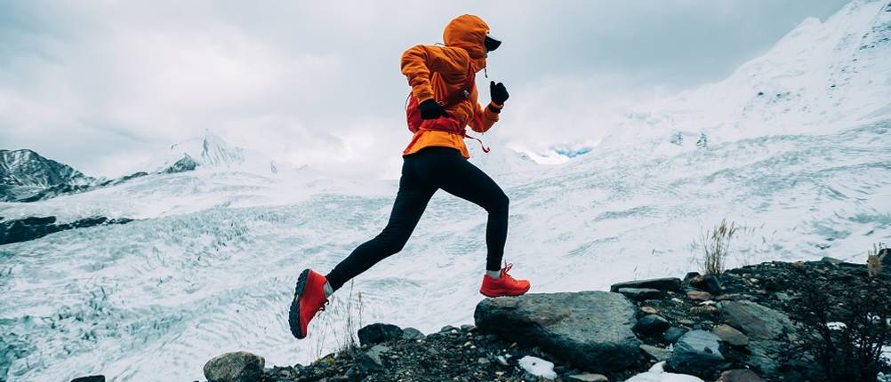 thermo-laufhose-damen-test: Eine Frau ist Funktionskleidung läuft einen verschneiten Berg hinauf. 