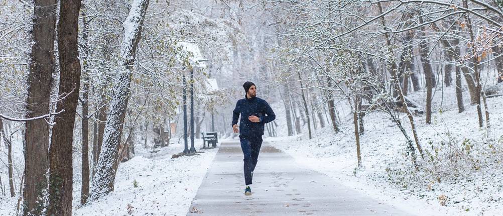 thermo-laufhose-herren-test: Ein Mann in Laufkleidung läuft durch eine verschneite Parklandschaft. 
