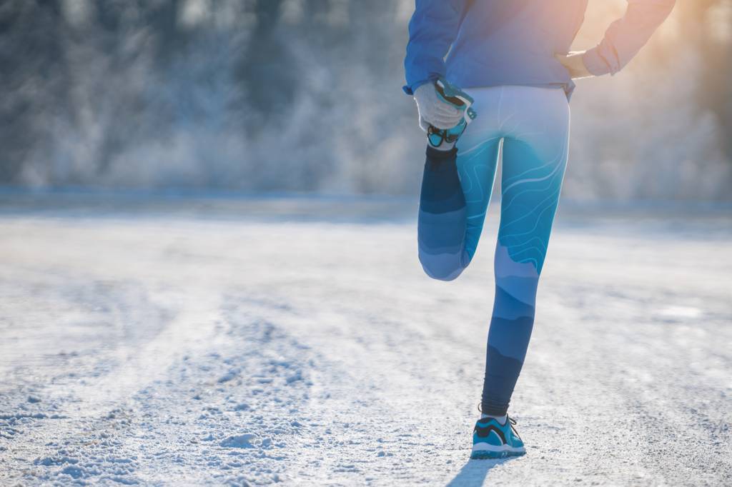 Thermo-Laufhose-Damen-Test: Eine Frau im Laufoutfit steht in einer verschneiten Landschaft und dehnt ihren Oberschenkel. 