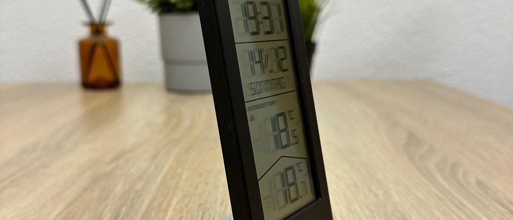 Ein Ade-WS2324-Thermometer steht schräg auf einem Tisch und zeigt die Displayanzeige aus einem seitlichen Blickwinkel.
