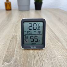 Ein Govee-H5075001DE-Thermometer steht aufrecht auf einem Holztisch und zeigt die aktuelle Temperatur sowie die Luftfeuchtigkeit auf dem Display an.