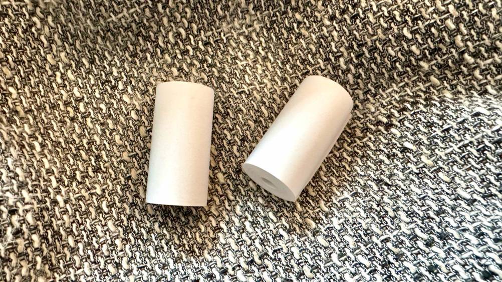 Zwei Rollen des Thermopapiers im Test auf der Seite liegend auf einem groben Stoff.