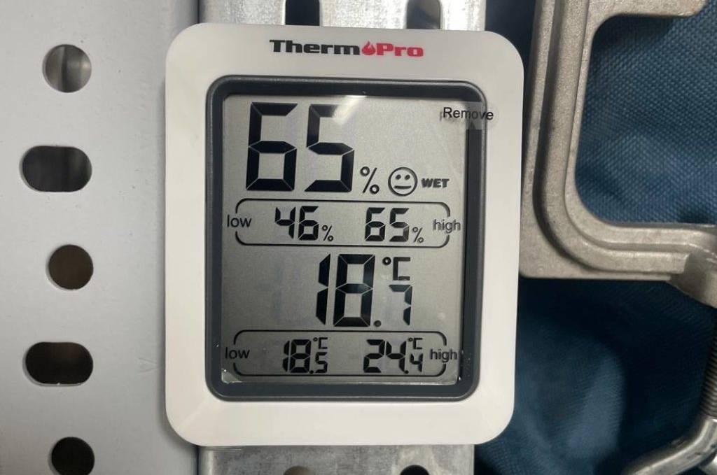 Nahaufnahme eines ThermoPro TP 50 Hygrometers im Test inklusive LCD-Anzeige, der an einem Metallregal hängt.