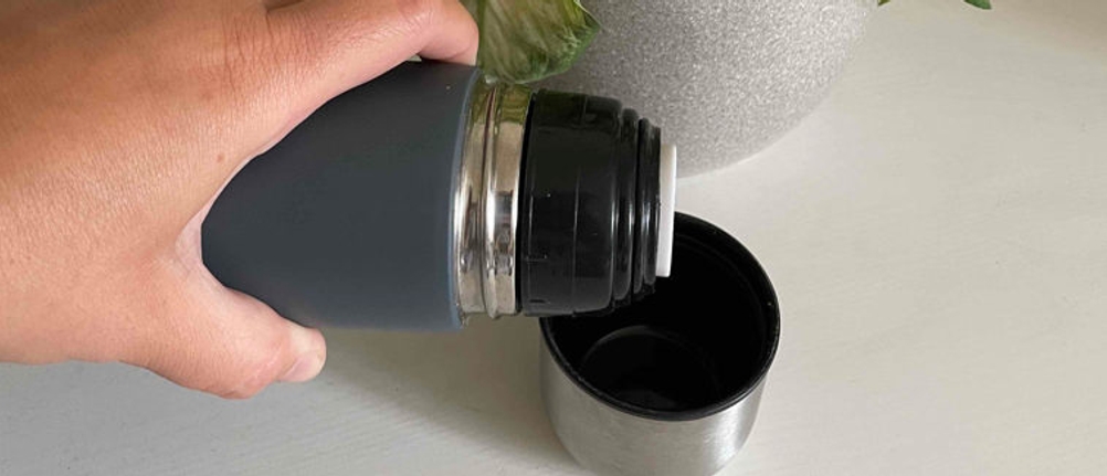 Eine Person gießt Flüssigkeit in den Becher einer Thermosflasche