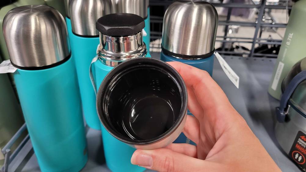 Eine Hand hält den Trinkdeckel einer getesteten Thermosflasche, mehrere Flaschen im Hintergrund.