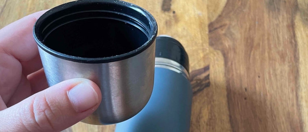 Eine Person hält den Becher einer Thermosflasche in der Hand