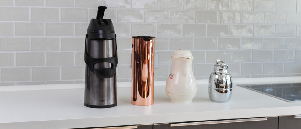 Vier Thermoskannen in unterschiedlichen Größen stehen nebeneinander auf einer Ablage.