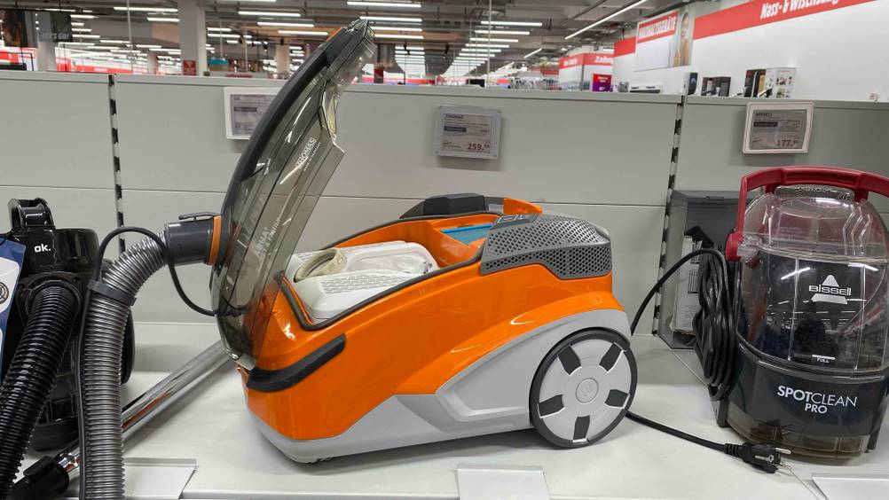 Ein getesteter Wasserstaubsauger mit geöffneter Klappe von schräg seitlich auf einem Verkaufsregal mit Preisangabe im Hintergrund.