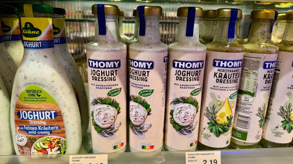 Mehrere Glasflaschen mit getestetem Thomy-Joghurt-Dressing stehen in einem Supermarktregal.