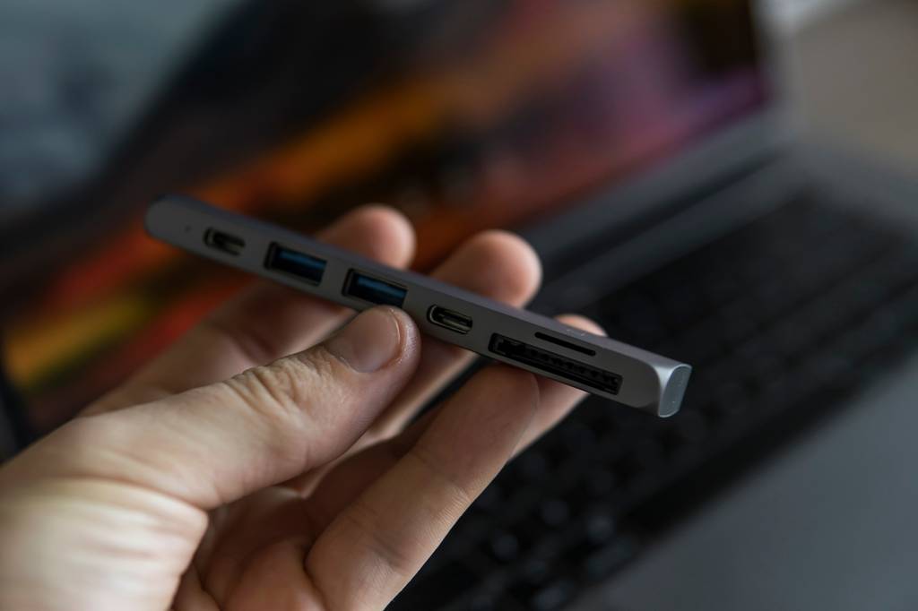 Thunderbolt-3-Dock im Test: Eine Hand hält ein Dock vor einem nur verschwommen erkennbaren Laptop.