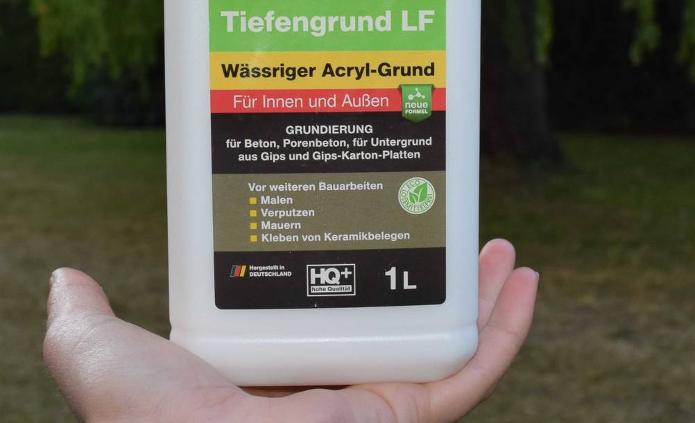 Nahaufnahme der Vorderseite einer Flasche des getesteten Tiefengrunds von einer Hand gehalten.