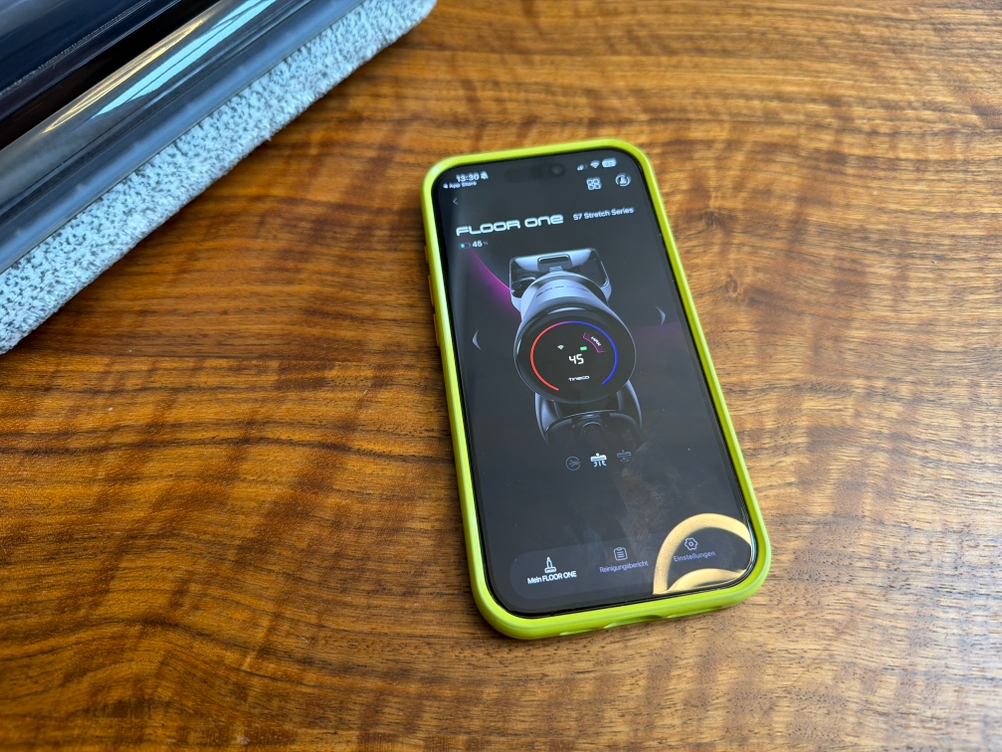 Ein Handy mit der App vom Tineco Floor One S7 liegt auf einem Holztisch