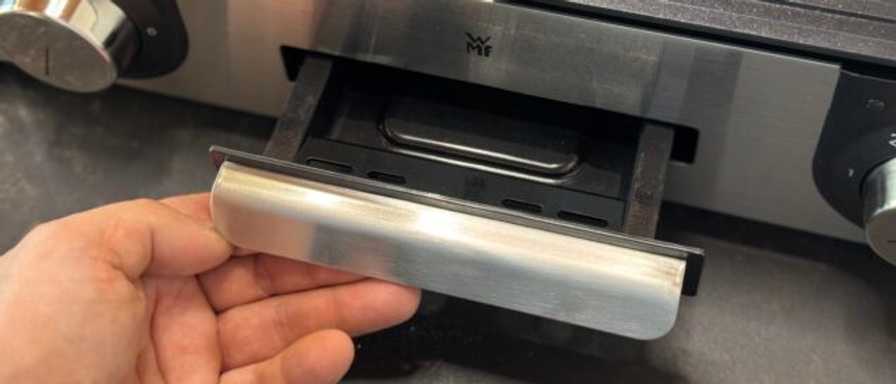 Eine Person nimmt die Auffangschale aus dem getesteten WMF-Tischgrill.