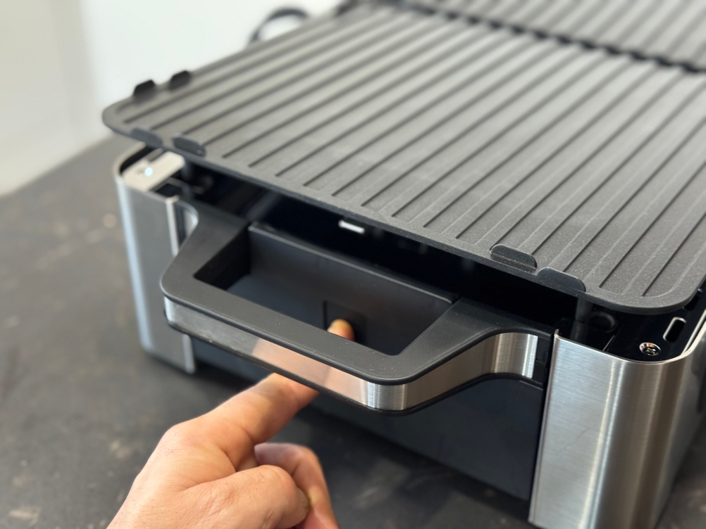 Eine Person drückt auf den seitlichen Knopf des getesteten WMF-Tischgrills, um die Grillplatte zu lösen.