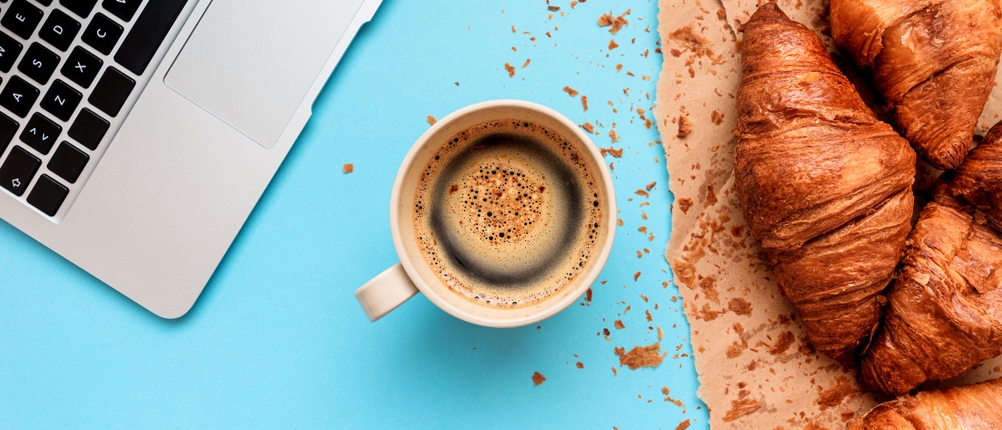 Ein verkrümelter Arbeitsbereich mit Kaffee, Croissants und einem Laptop