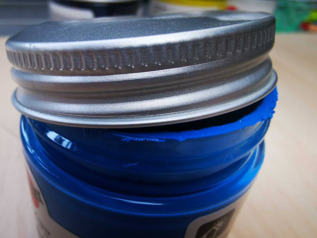 Der Schraubdeckel eines Glases getesteter Acryllack ist geöffnet.