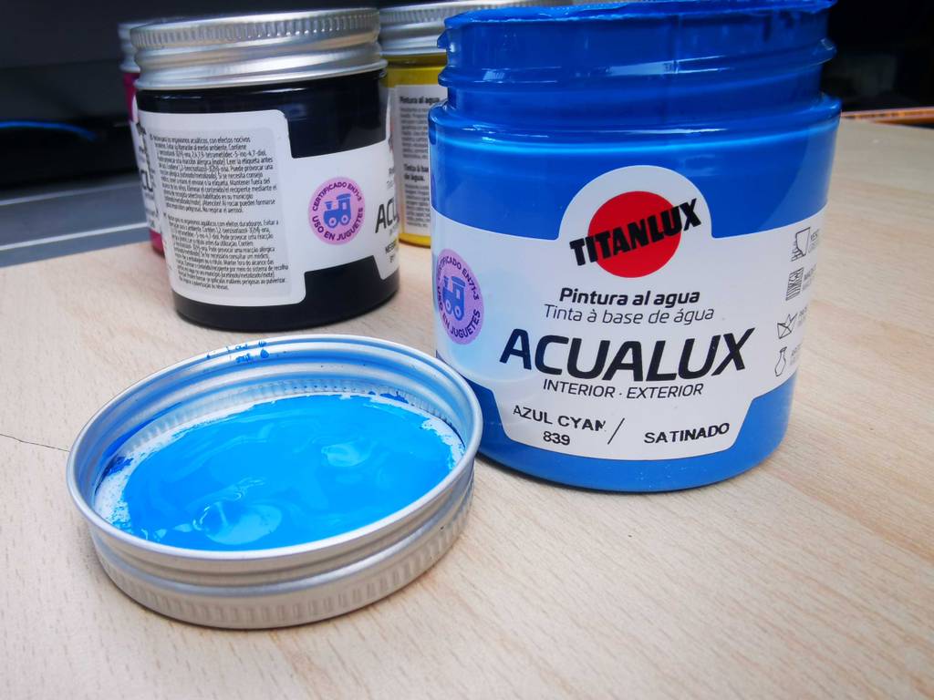 Der Deckel mit einem Klecks Farbe liegt neben dem Glas blauer getesteter Acryllack.