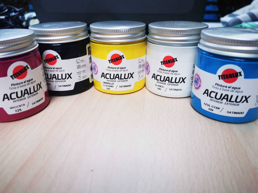 Acryllack im Test: Mehrere Gläser unterschiedlicher Farben sind auf einer hellen Fläche aufgereiht.