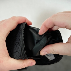 Ein TKMARS GPS Gerät wird in eine schwarze Fahrradtasche mit Reißverschluss gelegt. Zwei Hände halten Tasche und Tracker.