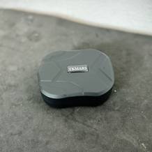 Das TKMARS GPS Gerät liegt auf einem grauen Untergrund. Die Oberseite ist schwarz und mit dem Markenlogo versehen.
