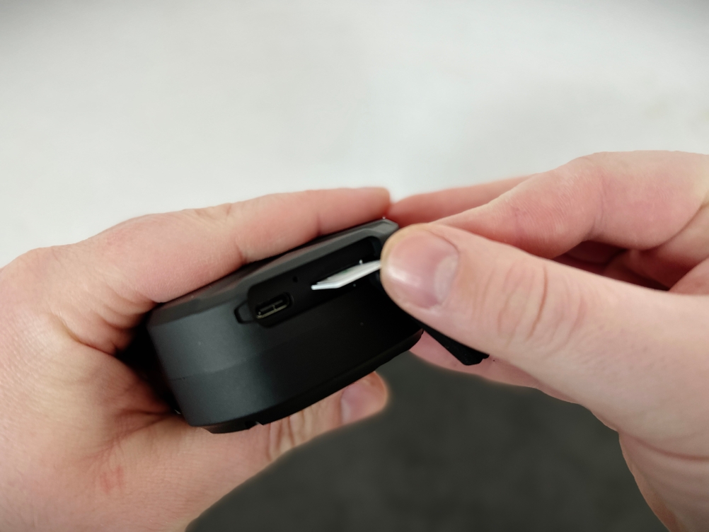 Eine Hand führt eine SIM-Karte in den Kartenschlitz des TKMARS GPS Geräts ein. Daneben befindet sich der Ladeanschluss.