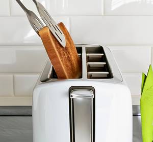 Toaster-mit-Sandwichzange-Test: Ein Toast-Brot wird mit einer Metall-Zange aus einem weißen Toaster geholt. 