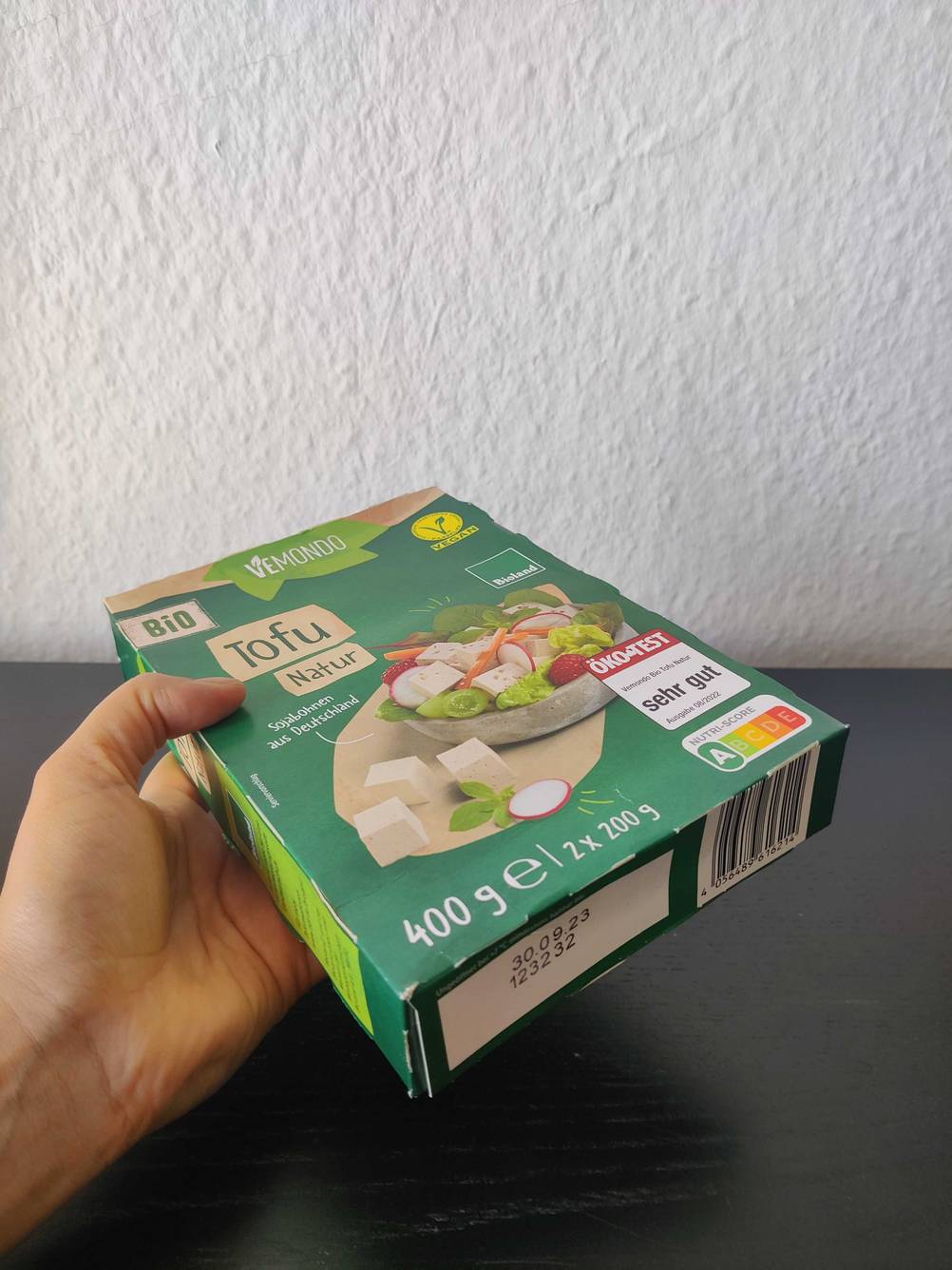 Eine Hand hält eine Packung des Tofus im Test mit Fokus auf den Boden.