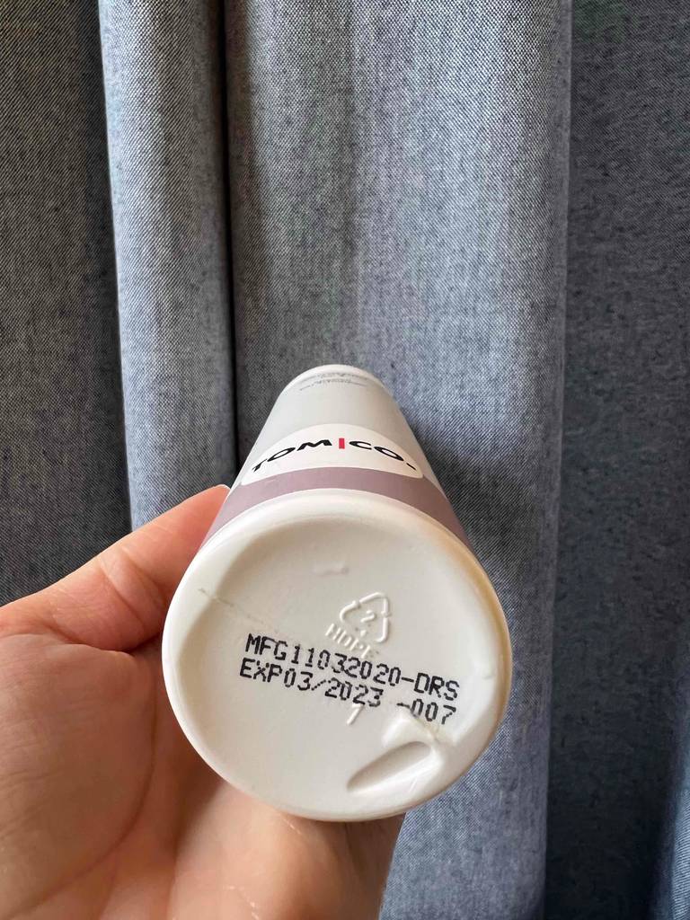 Eine Hand hält den Boden des getesteten Antischuppenshampoos vor einen grauen Vorhang.