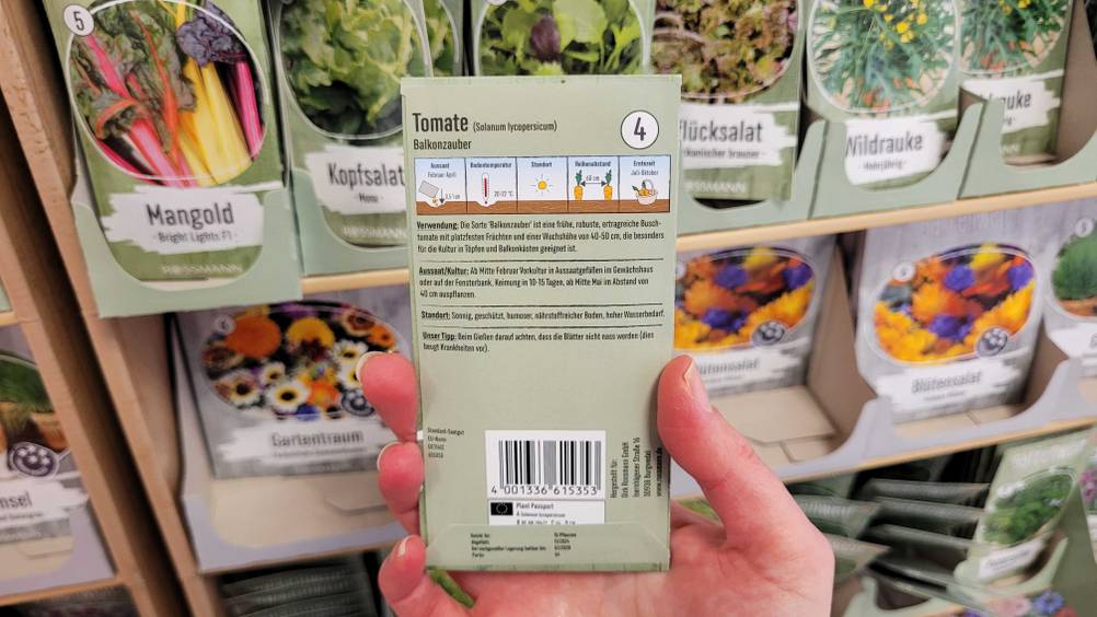 Die Rückseite der getesteten Tomatensamen von einer Hand vor ein Regal gehalten.