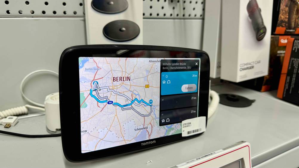 Ein getestetes TomTom-Navi von schräg seitlich auf einem Regal mit anderen Produkten.