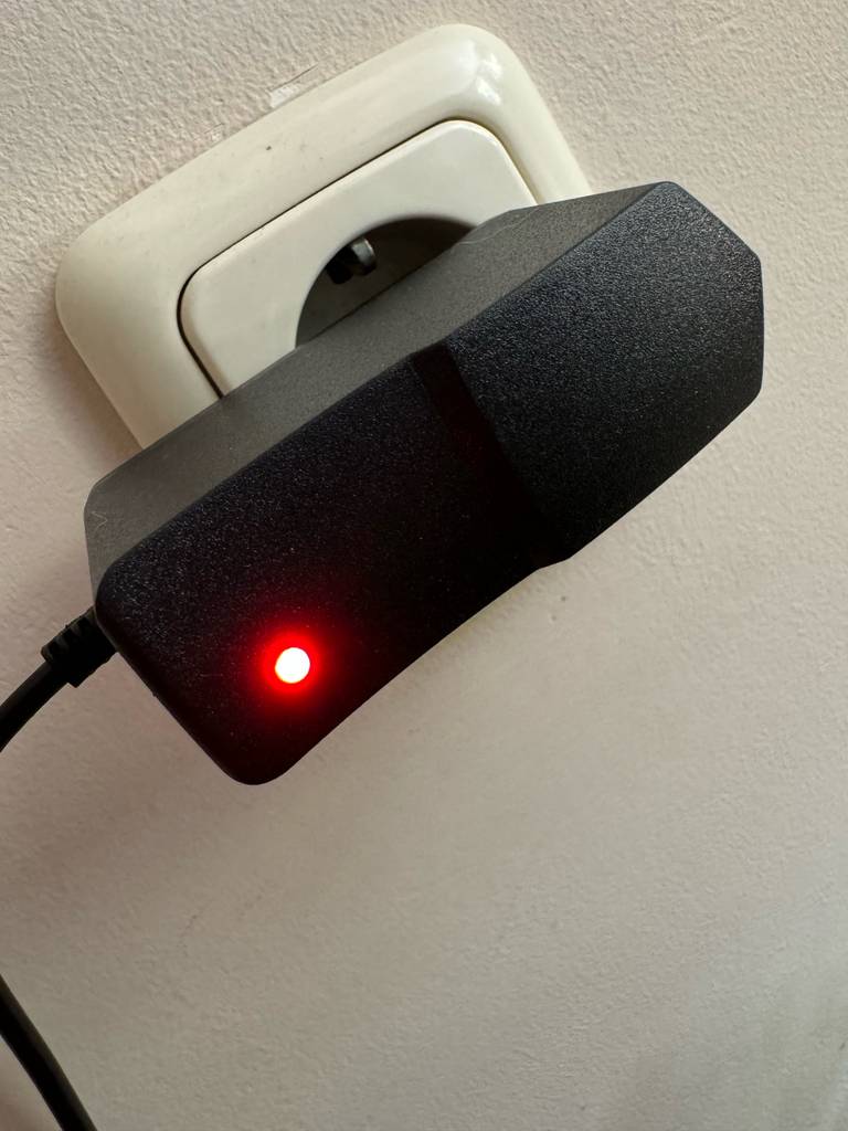 Funkmikrofone im Test: Nahaufnahme eines in der Steckdose eingesteckten, schwarzen Adapters inklusive eingeschalteter LED-Leuchte.